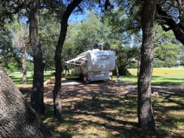 white goose-neck rv traeler parked on site. Lots of oak trees and shade on a sunny day